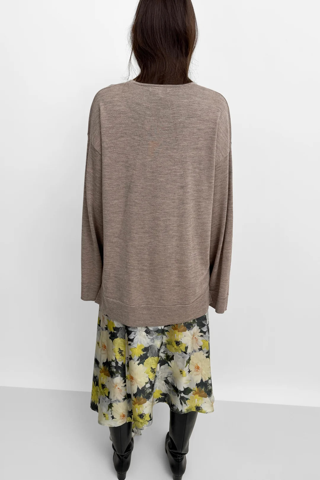 A model shown from the back wearing a taupe-brown long-sleeve knit top and a yellow, white, and green floral print skirt, paired with black boots, against a plain white studio background.