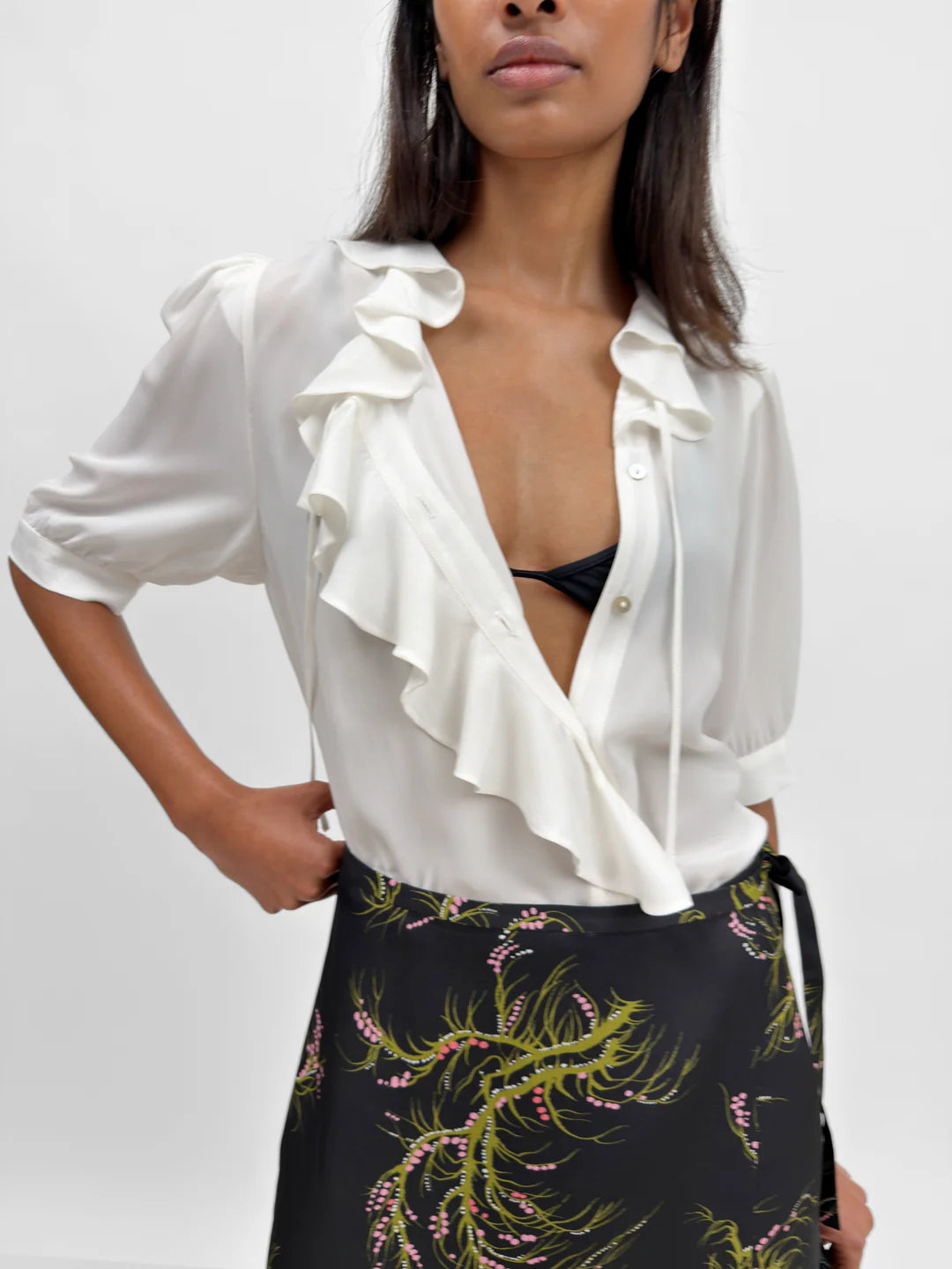 Woman wearing a white ruffled blouse over a black floral skirt on a plain background