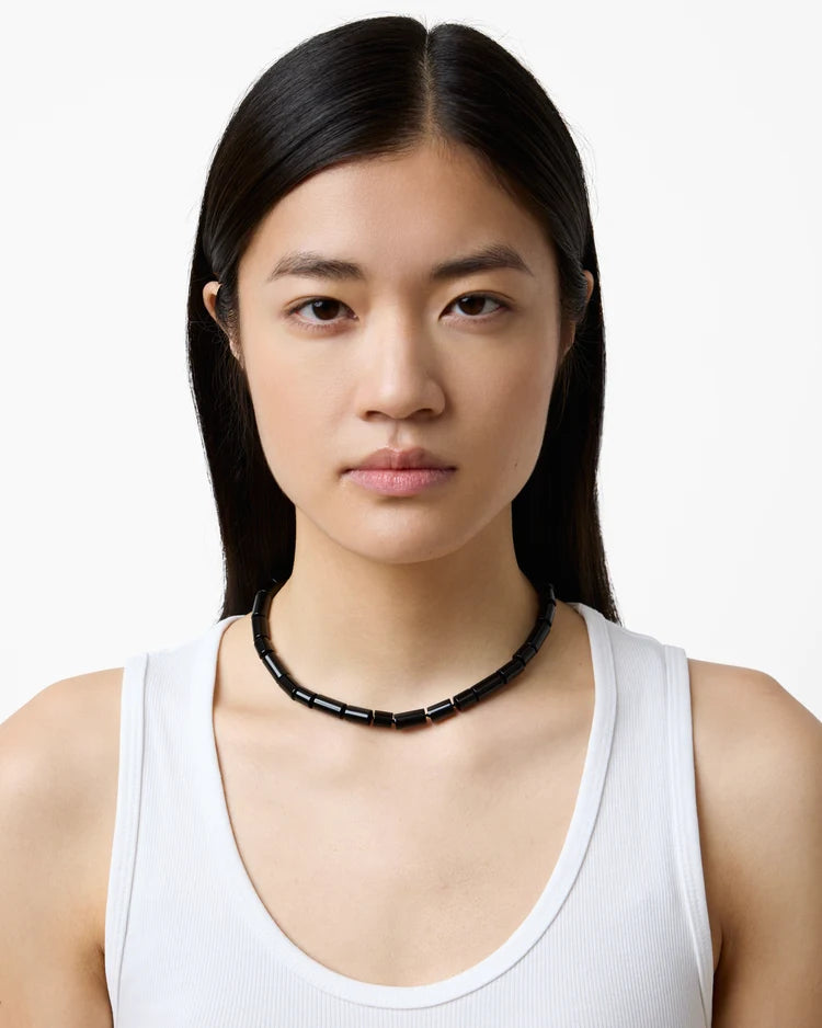 Woman wearing a white tank top and black beaded necklace on a white background