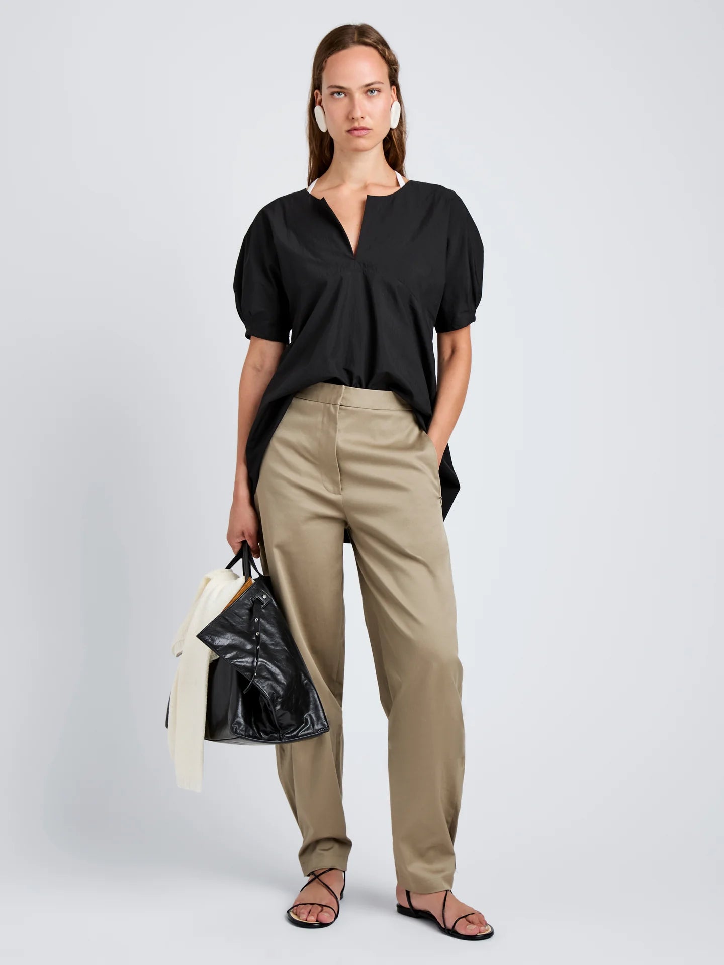 Woman wearing a black top and beige pants, holding a black bag on a white background