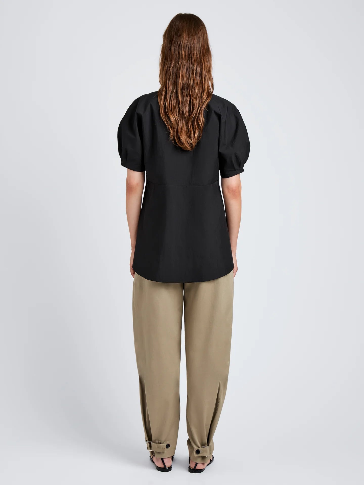 Woman wearing a black top and beige pants on a white background
