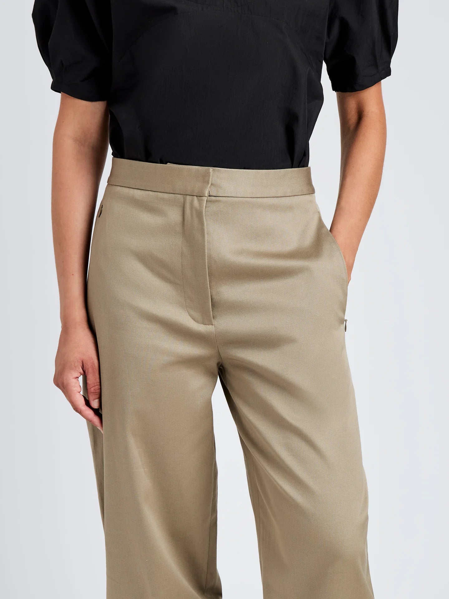 Person wearing beige pants and a black top on a light gray background