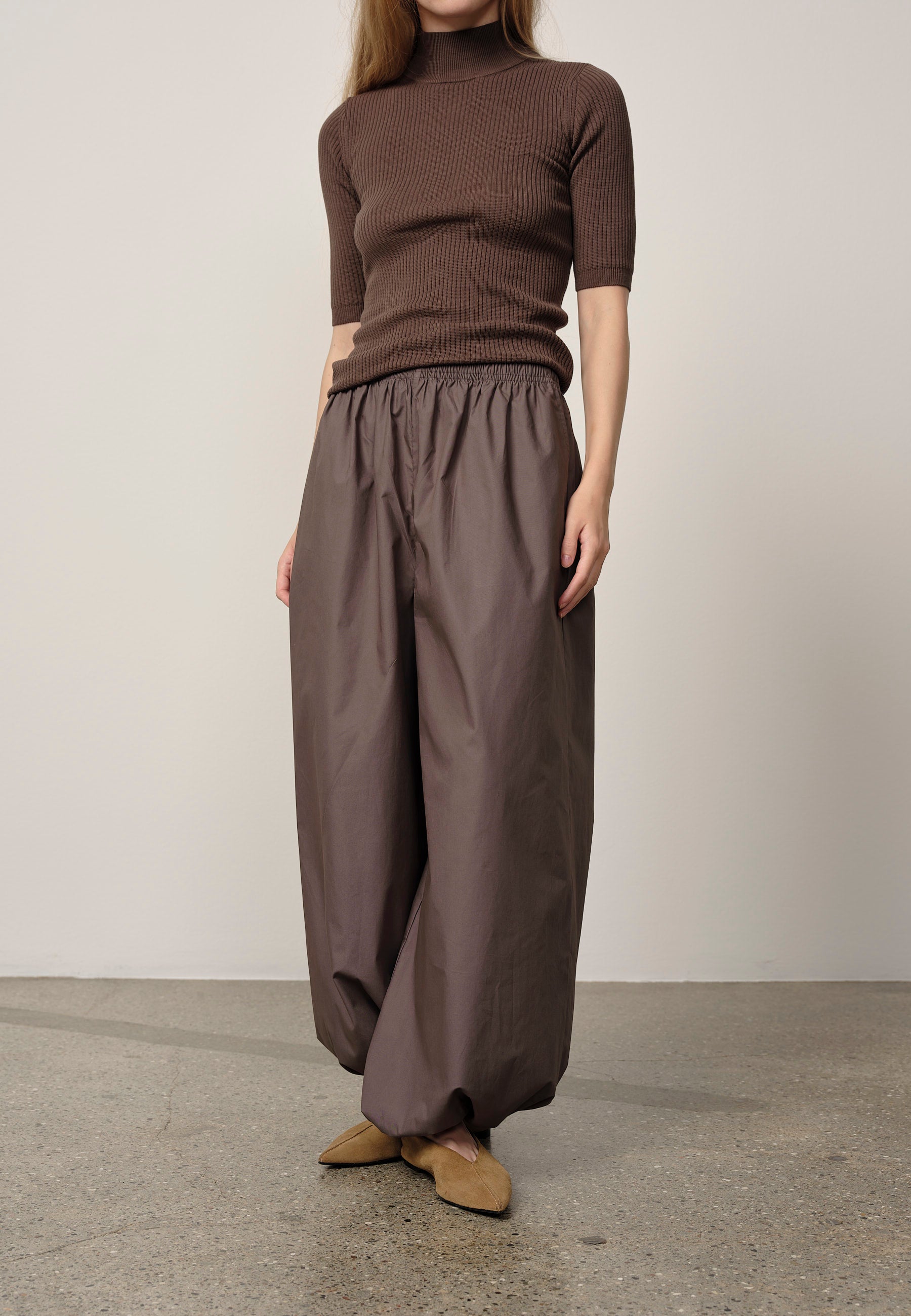 Person wearing a brown ribbed sweater and wide-leg pants standing against a plain background