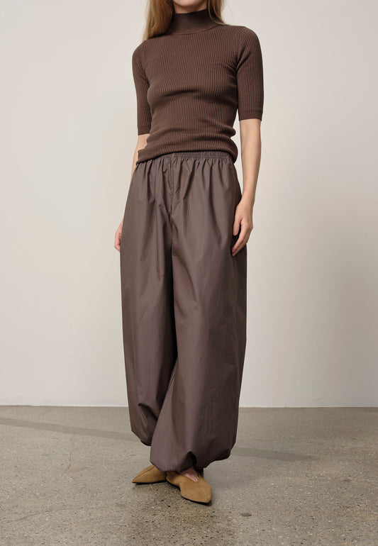 Person wearing a brown ribbed sweater and wide-leg pants standing against a plain background