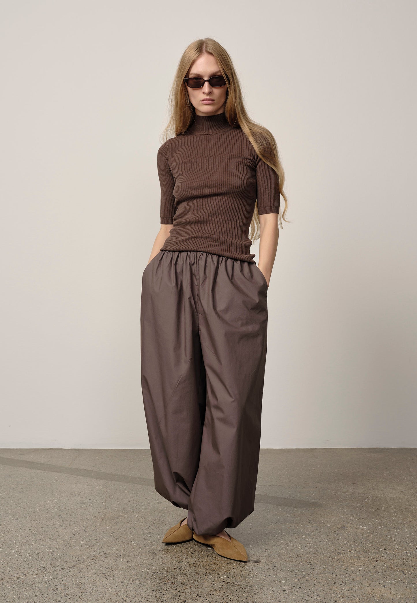 Woman wearing a brown turtleneck and wide-leg pants against a plain background