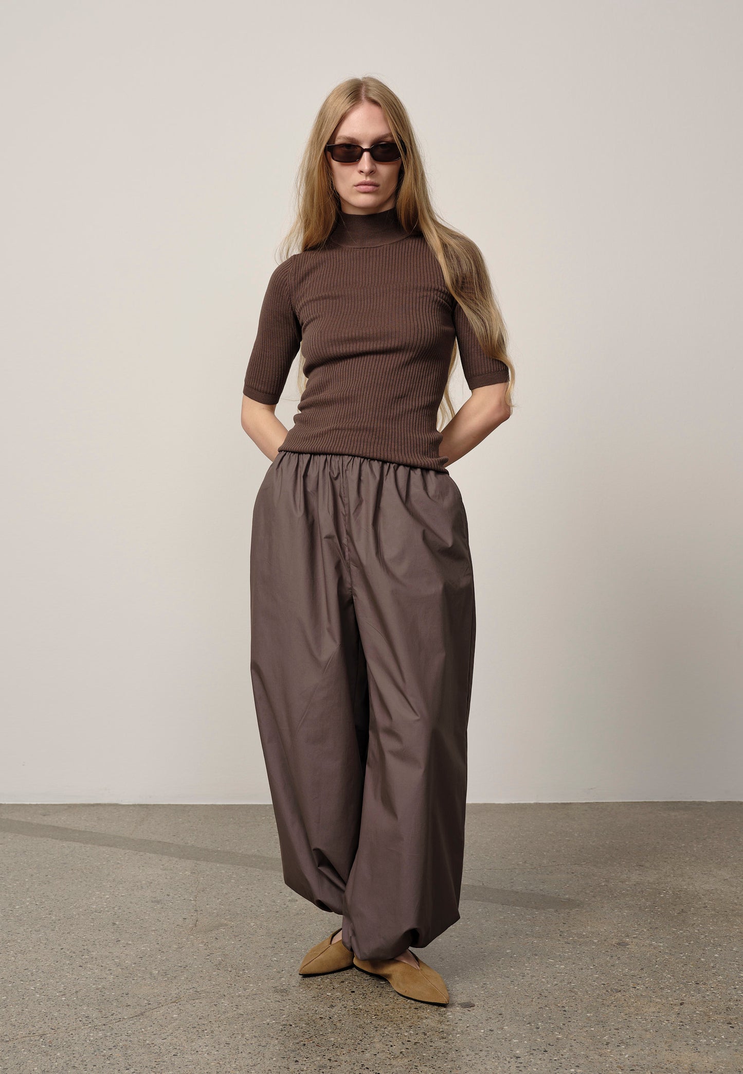 Woman wearing a brown outfit with sunglasses against a plain background