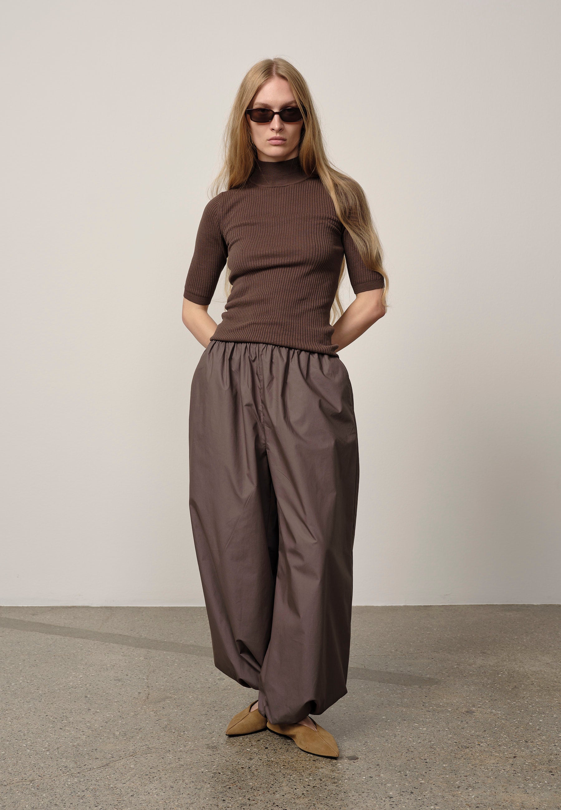 Woman wearing a brown outfit with sunglasses against a plain background