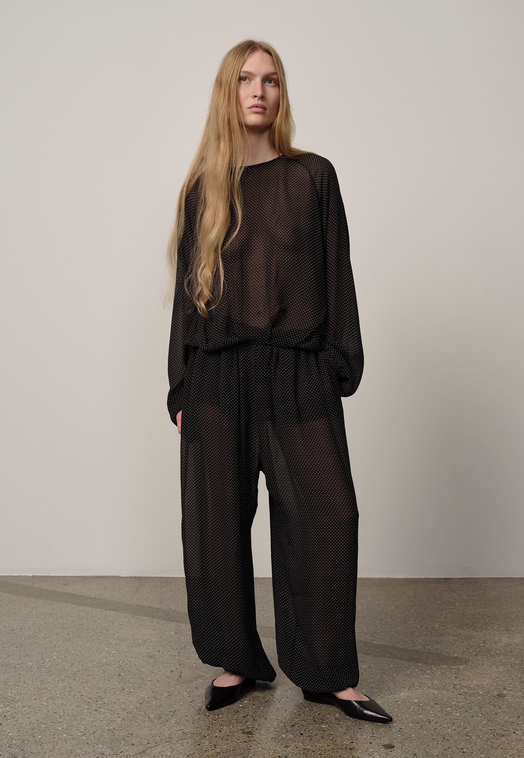 Person wearing a black outfit with sheer elements on a plain background