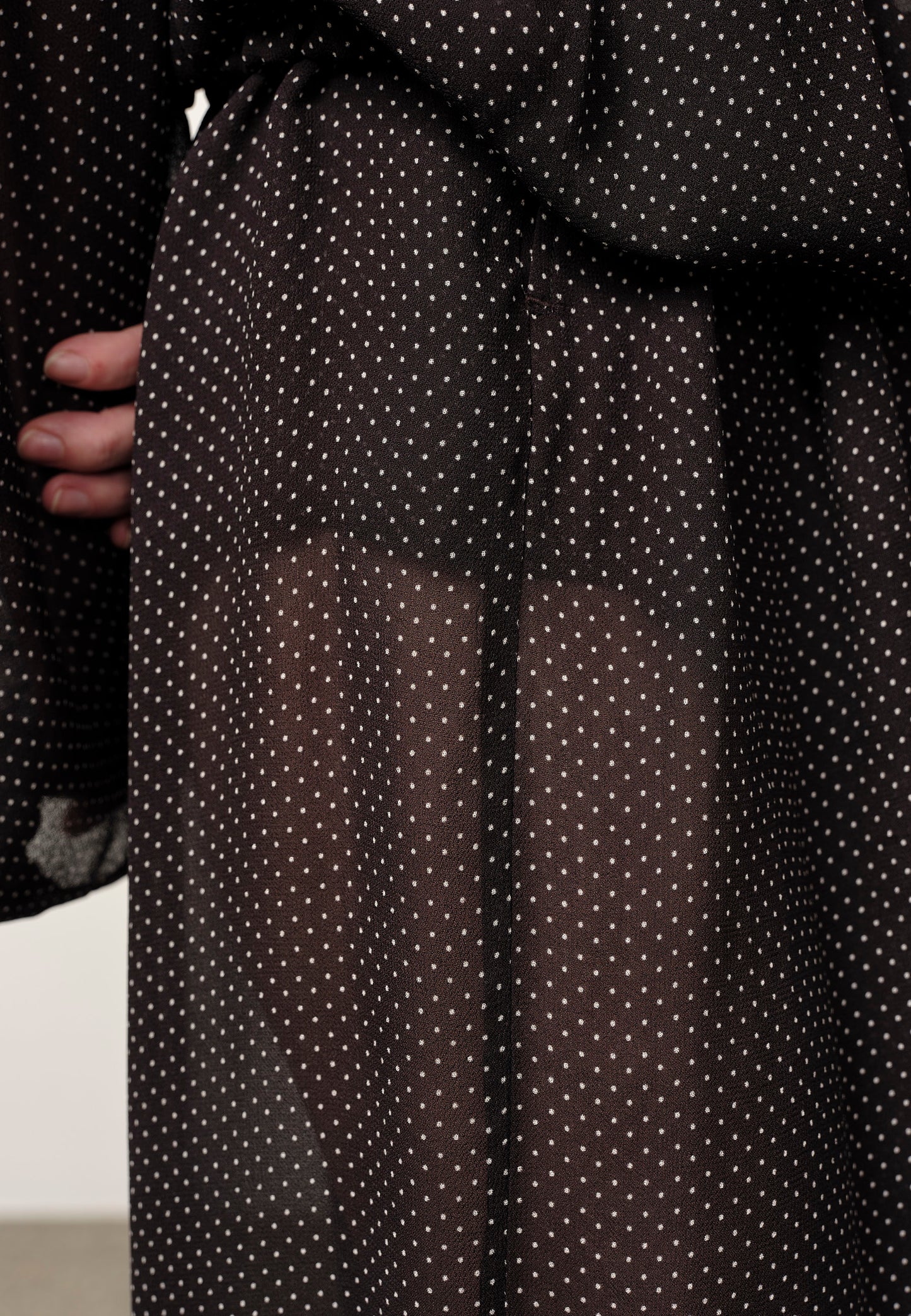 Black polka dot sheer fabric held by a person against a neutral background
