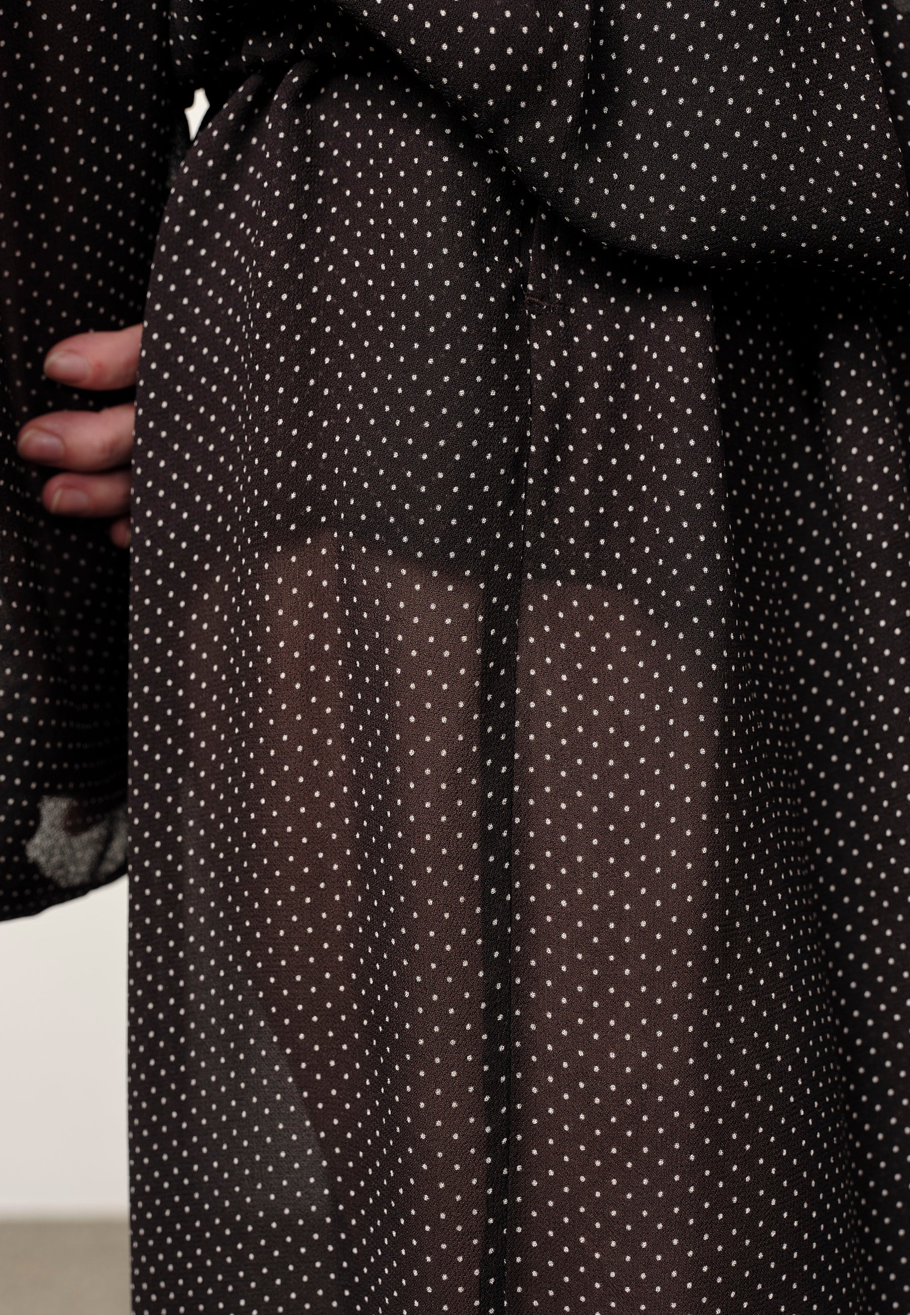 Black polka dot sheer fabric held by a person against a neutral background