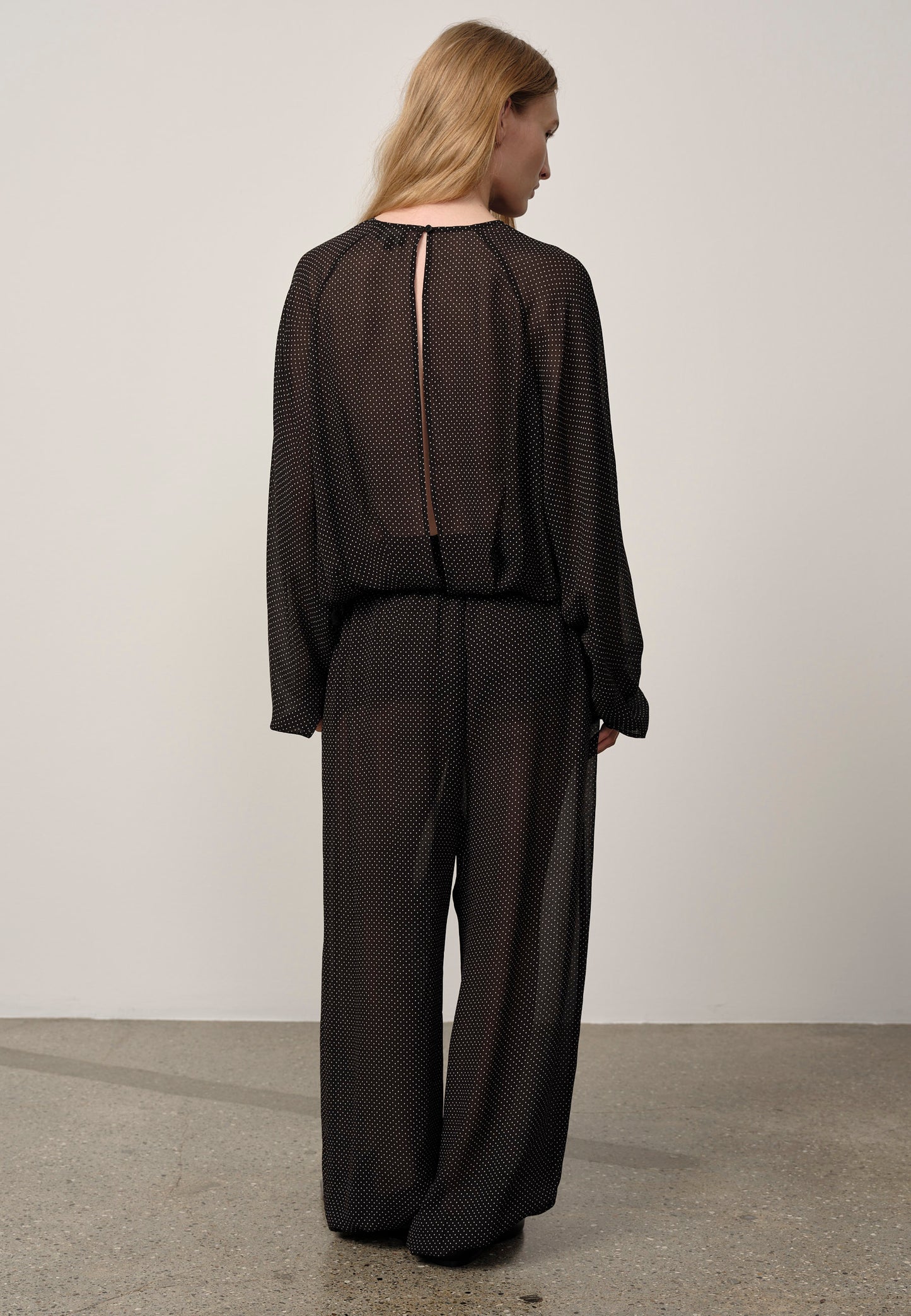 Person wearing a black outfit with sheer details on a plain background