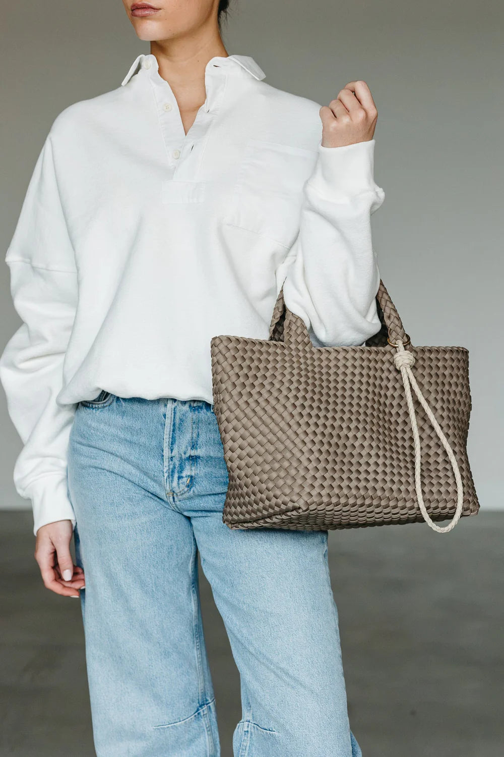 Person wearing a white shirt and blue jeans holding a woven brown bag.
