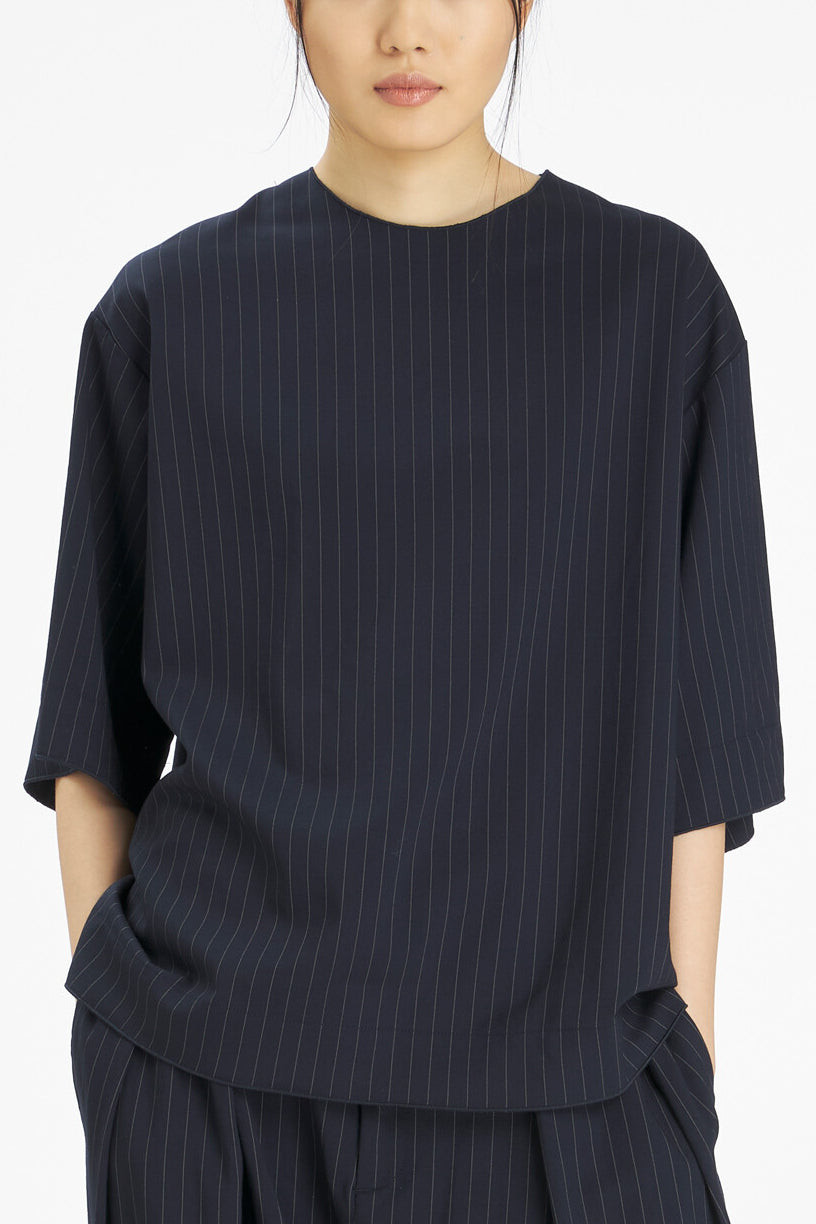 A model wearing a dark navy blue short-sleeve top with thin vertical pinstripes, paired with matching pinstriped pants, against a clean white background.