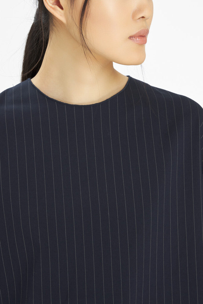 Close-up of a person wearing a dark navy top with thin vertical pinstripes against a plain light background.