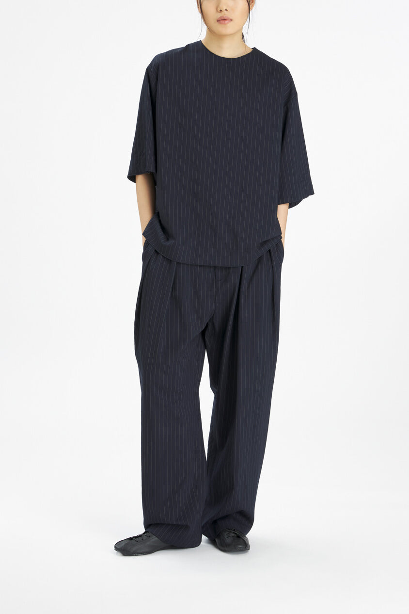 A model wearing a dark navy blue ribbed two-piece outfit consisting of a short-sleeve top and matching wide-leg trousers, paired with black shoes, against a plain white studio background.