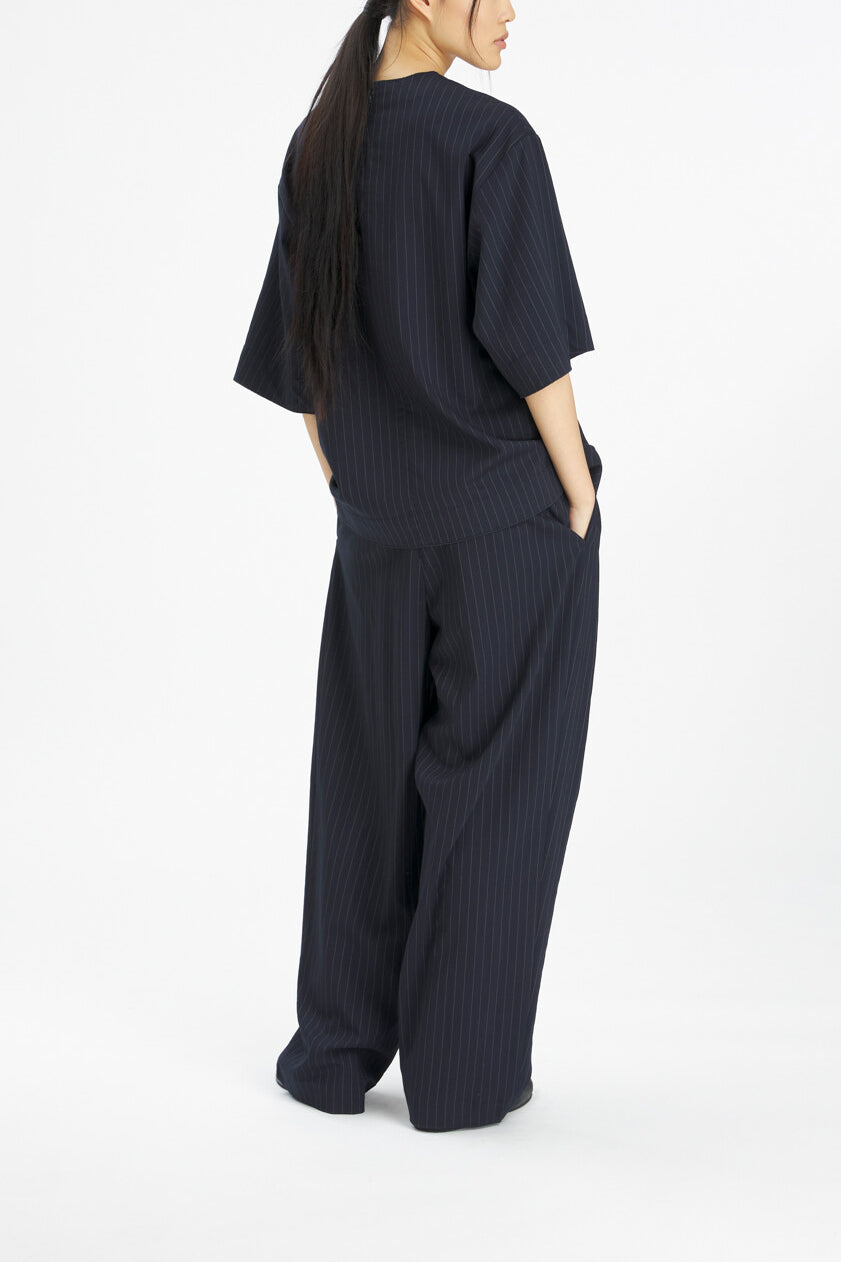 A model shown from the back wearing a dark navy blue ribbed two-piece set consisting of a short-sleeve top and wide-leg trousers, against a plain white studio background.