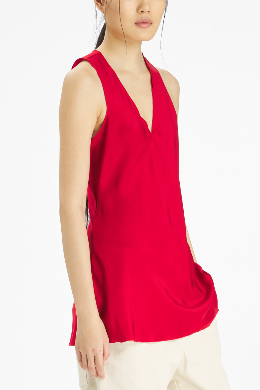 A model wearing a bright red sleeveless wrap-style top with a deep V-neckline, paired with light beige pants, photographed against a clean white studio background.
