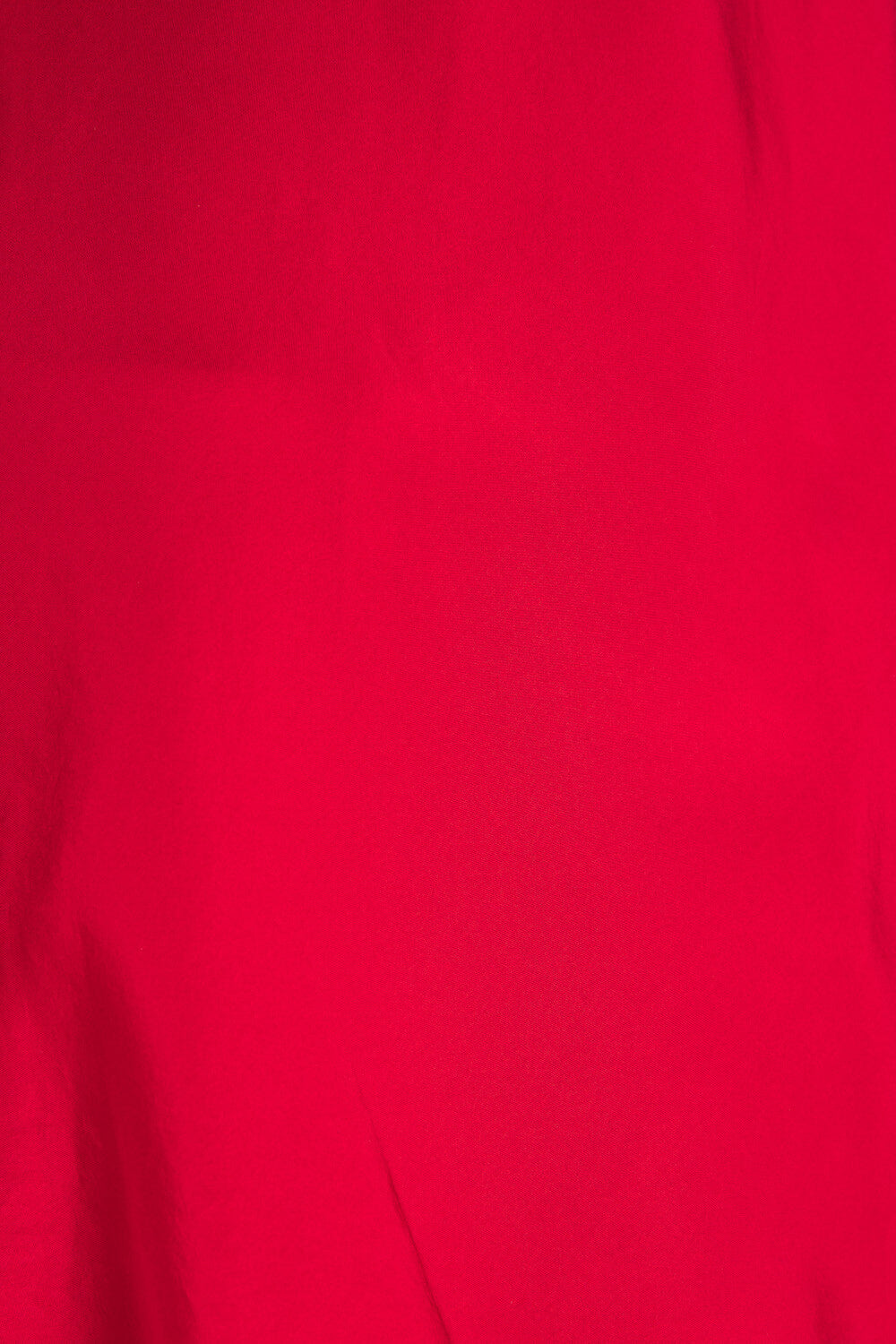 A close-up of bright red fabric with soft folds and a smooth texture.