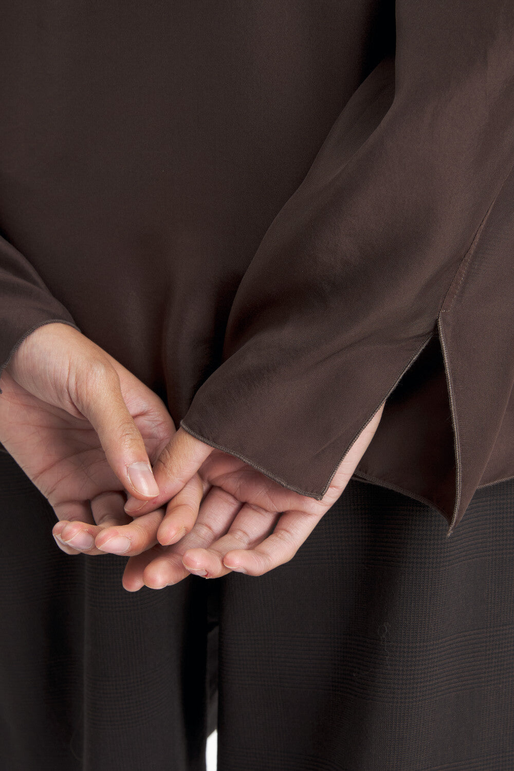 Close-up of a person wearing a dark brown long-sleeve top or robe, with both hands folded together in front of the torso.
