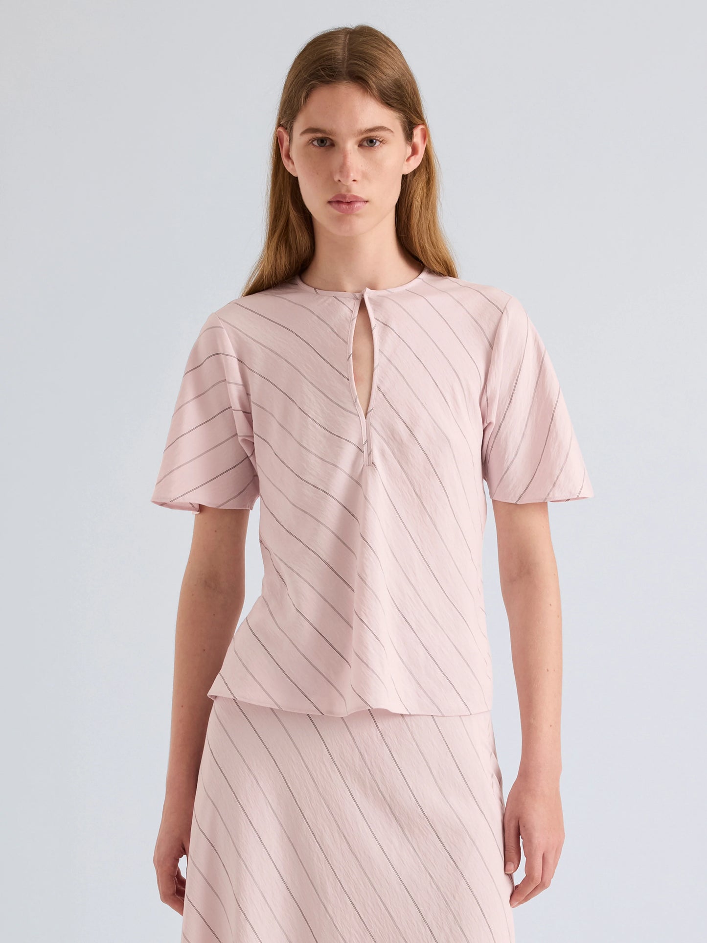 Woman wearing a light pink dress with a subtle pattern on a plain background