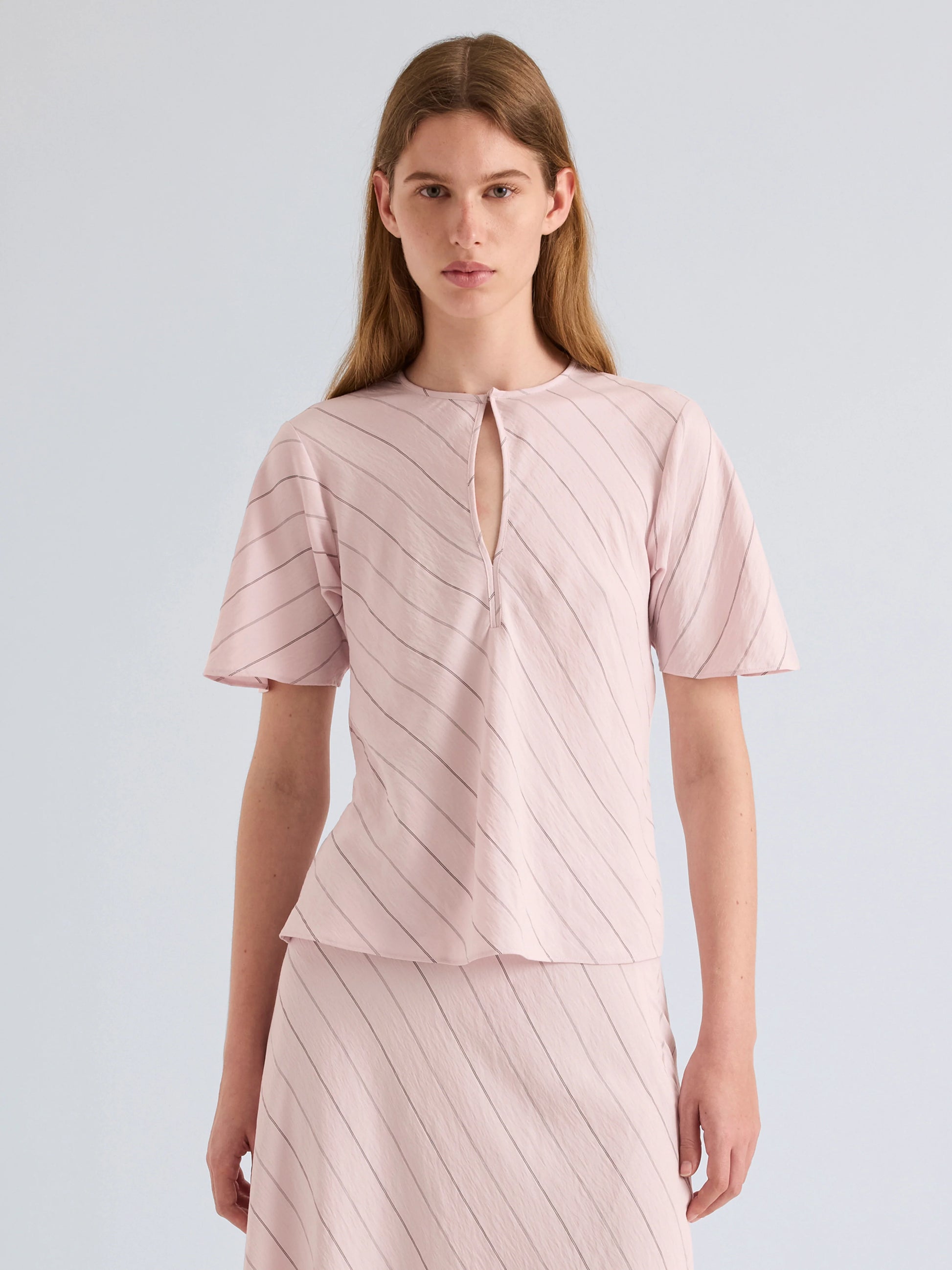 Woman wearing a light pink dress with a subtle pattern on a plain background
