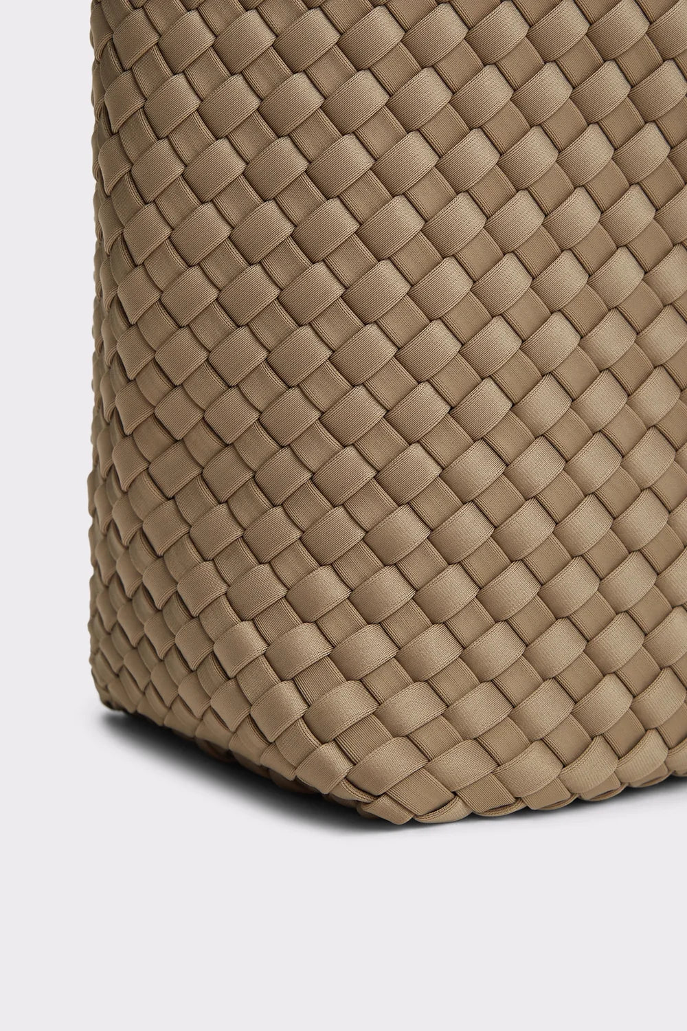 Close-up of a woven leather bag corner in a warm taupe-beige color, showing the detailed basketweave texture and stitched edge against a light gray background.
