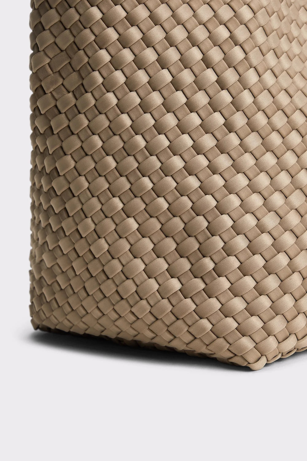 Close-up of a woven leather bag corner in a light taupe-beige color, showing the detailed basketweave texture against a light gray background.