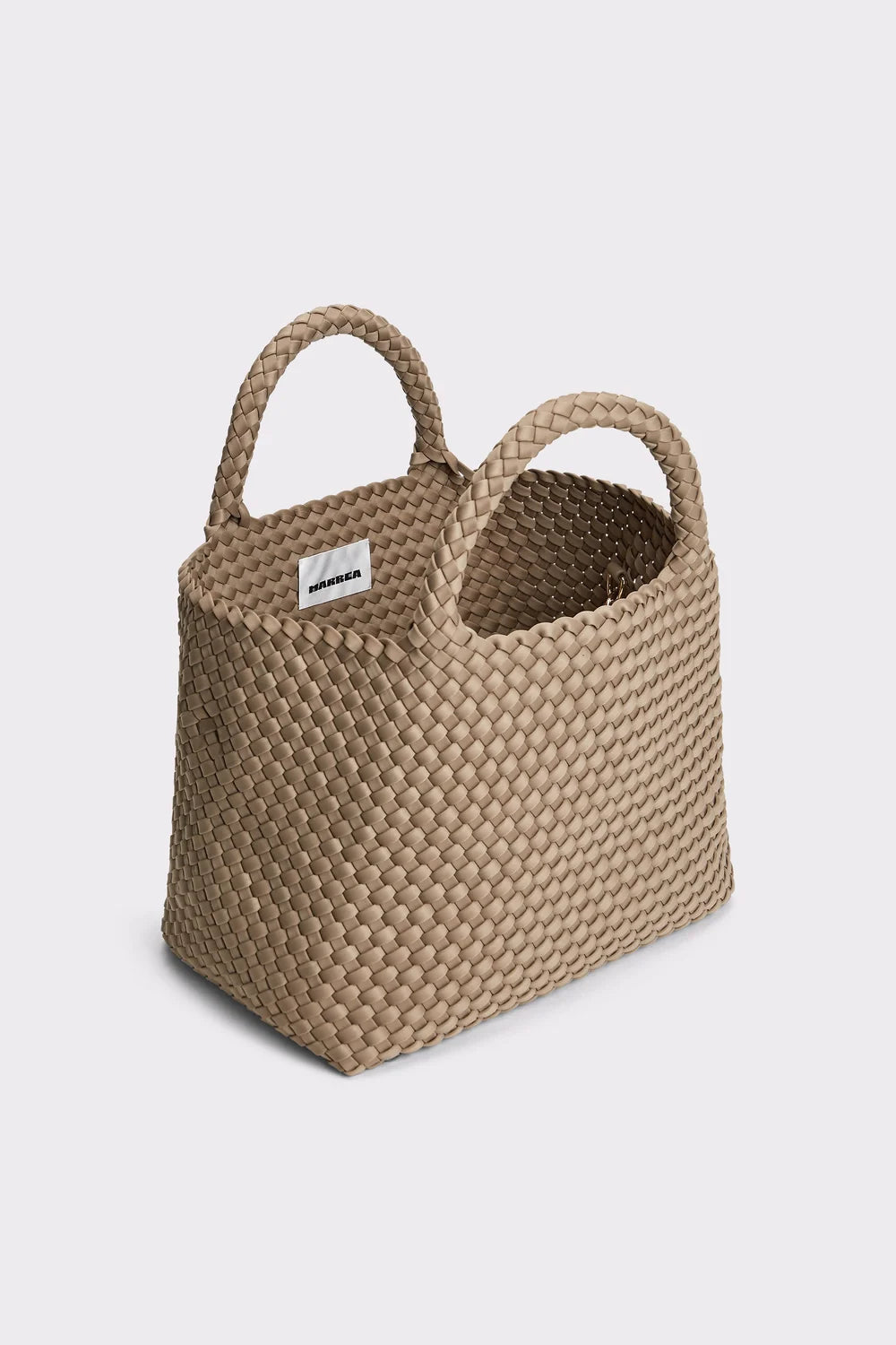 A woven straw tote bag in a natural beige color, featuring two integrated top handles and a small white brand label on the side, set against a plain light gray background.