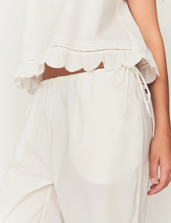 Close-up of a white dress with scalloped hem and ribbon detail on a plain background
