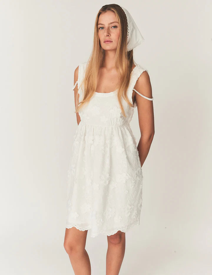 Woman wearing a white dress with sheer sleeves against a plain background