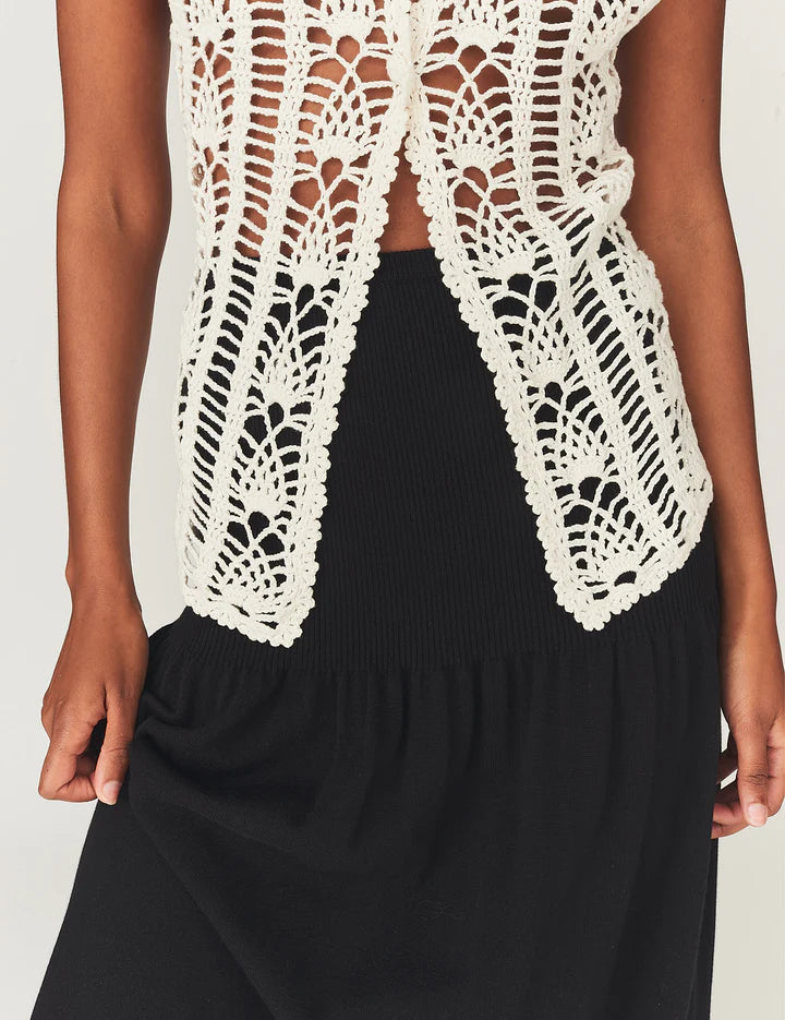 White lace top over a black outfit on a plain background
