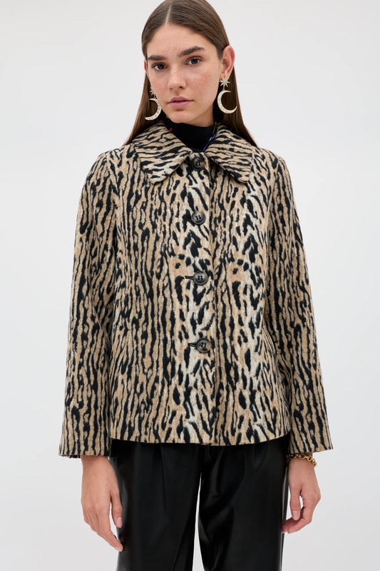 A model wearing a beige and black leopard-print cropped jacket with a wide collar and front buttons, paired with black pants, against a plain light gray background.