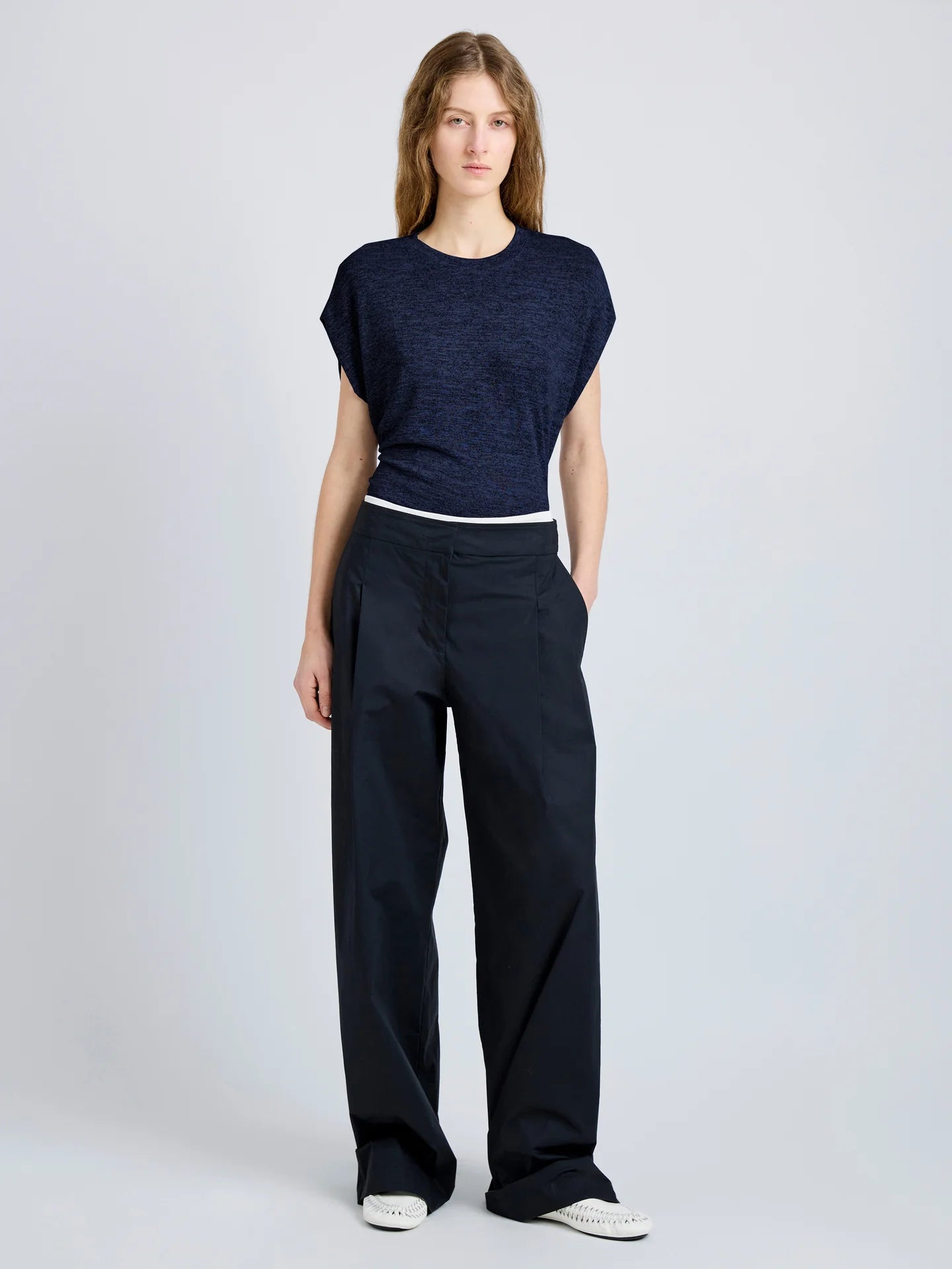 Woman wearing a navy blue top and black pants on a light gray background