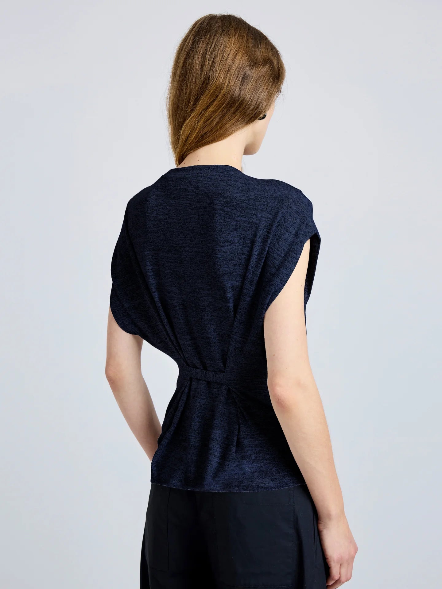 Woman wearing a dark blue top with a knot detail on a light gray background