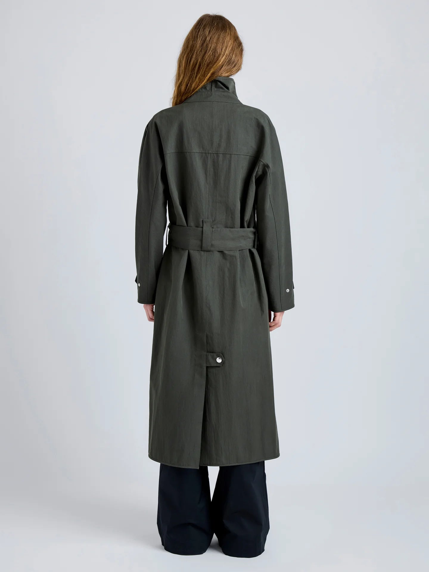 Person wearing a long dark green coat on a light gray background