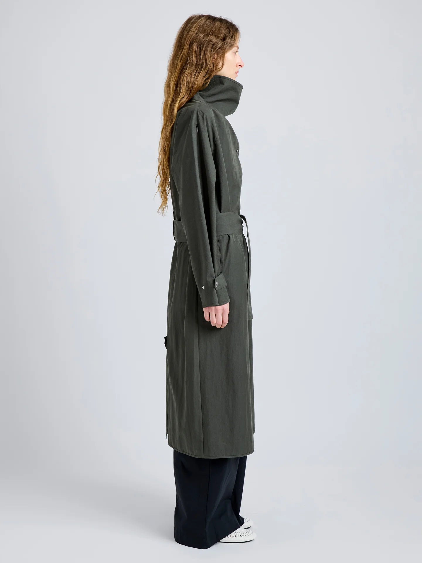 Person wearing a long dark green coat on a light gray background