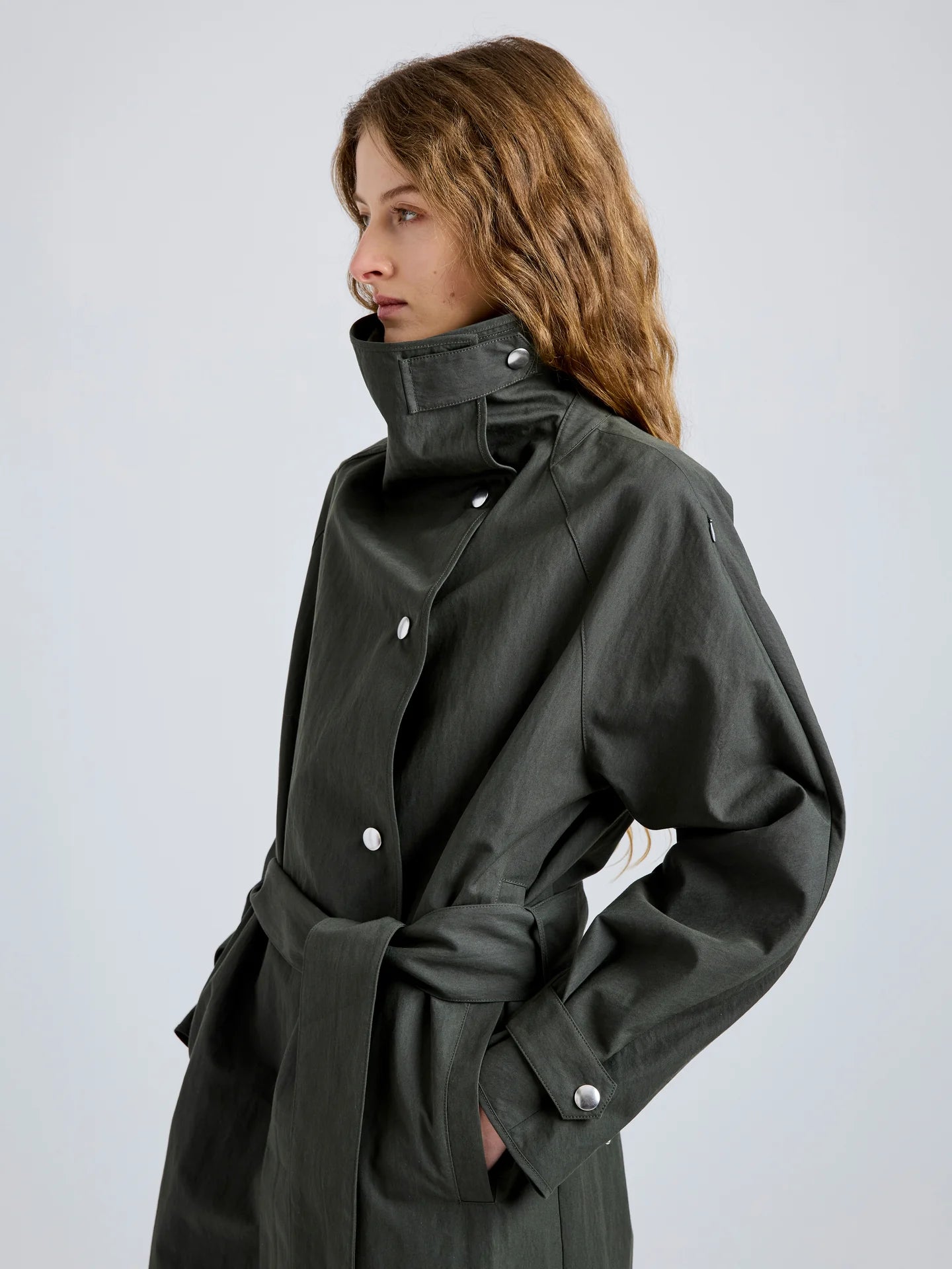 Person wearing a  dark green coat on a light gray background