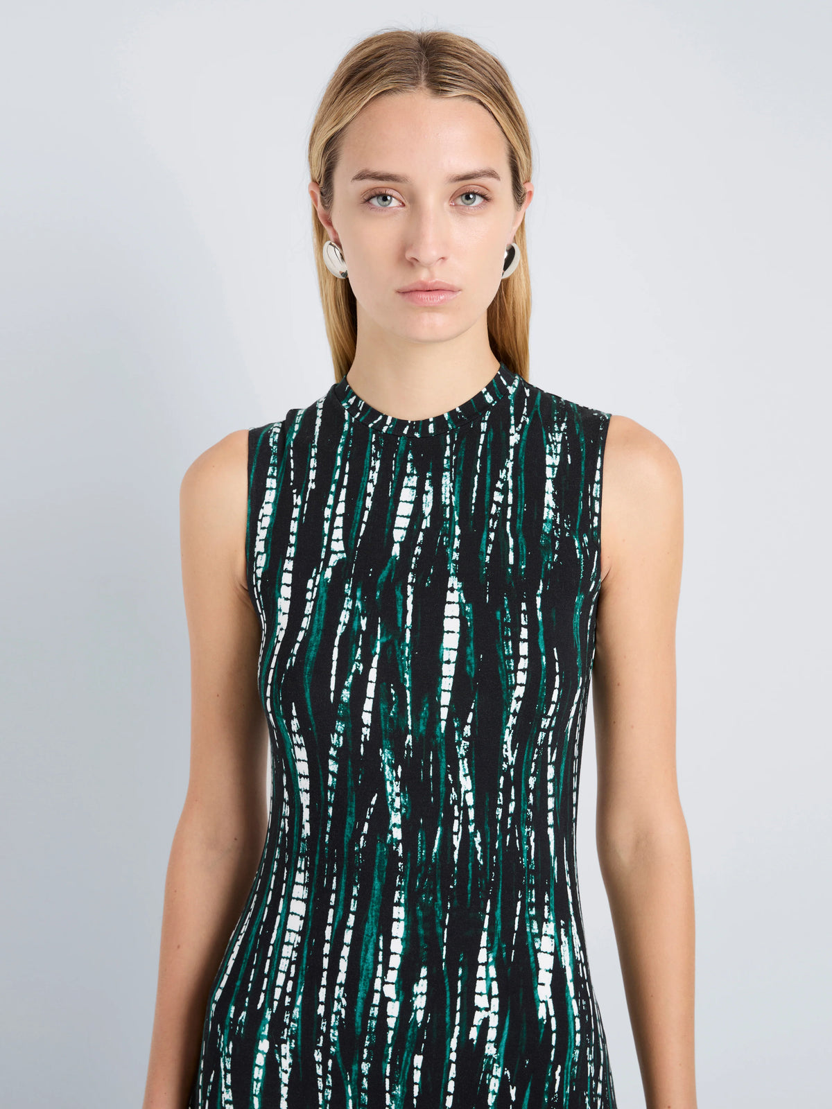 Woman wearing a sleeveless dress with a green and black pattern on a gray background