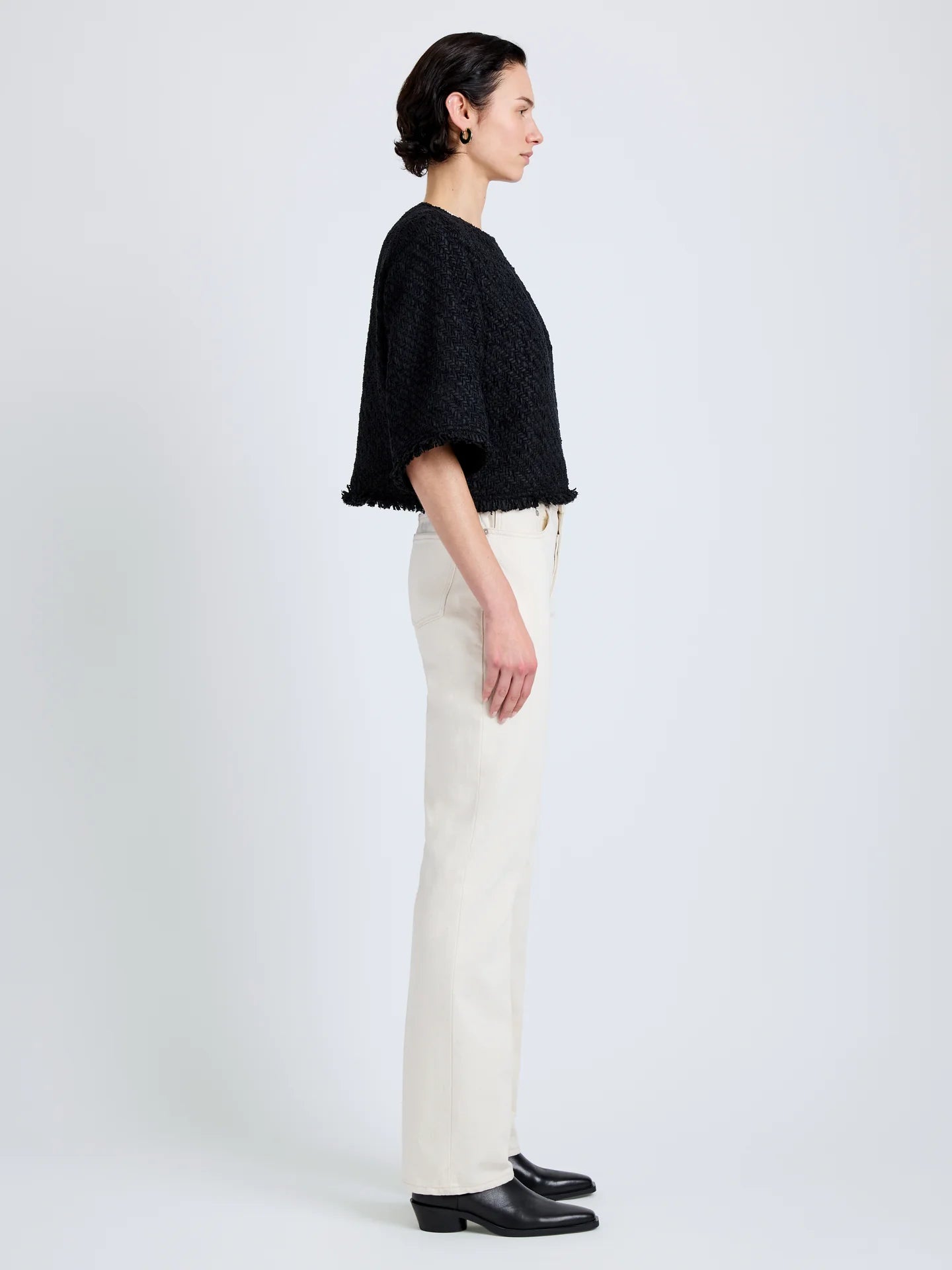 Woman wearing a black top and white pants on a plain background