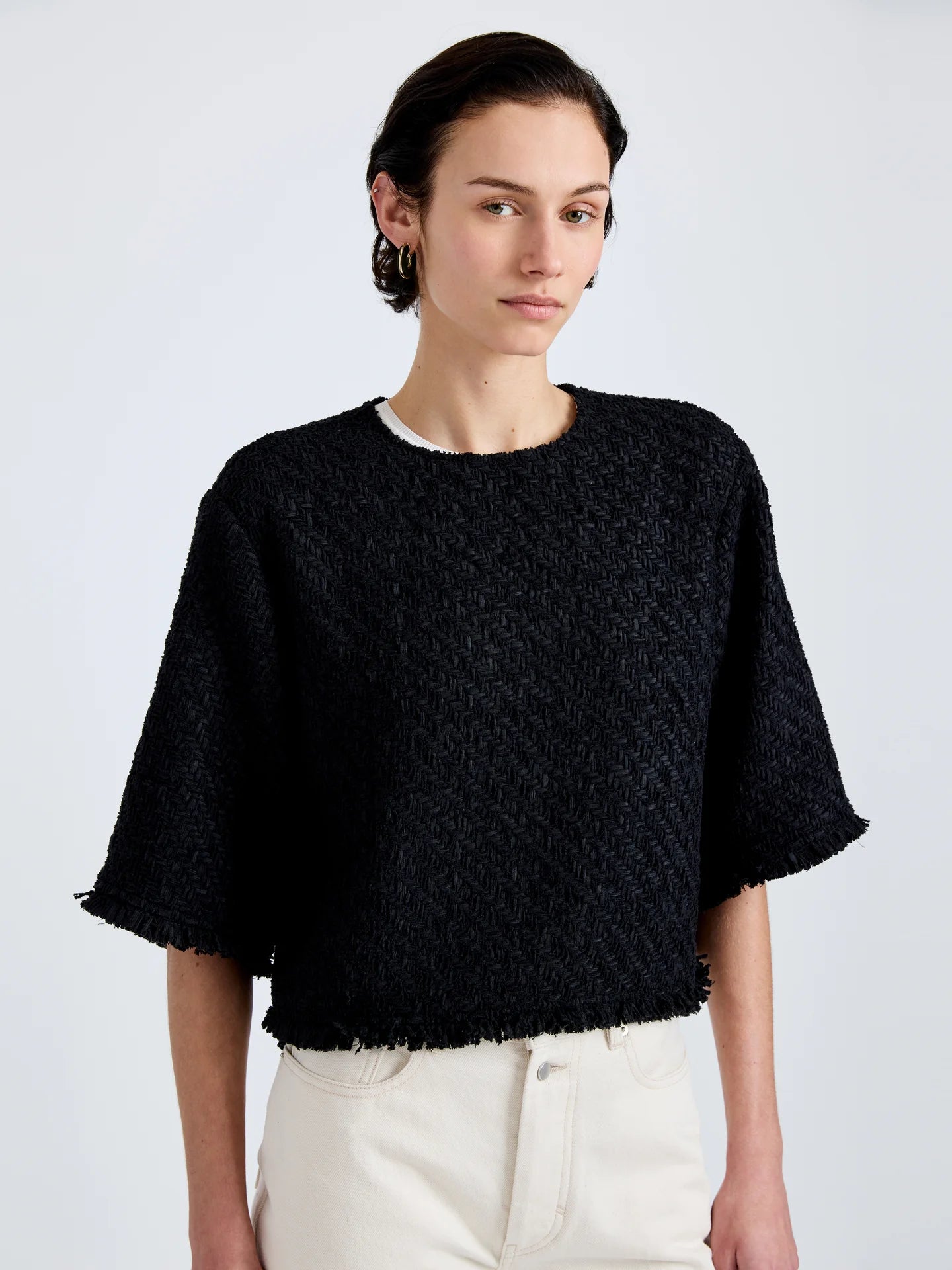 Woman wearing a black textured sweater and white pants on a light gray background