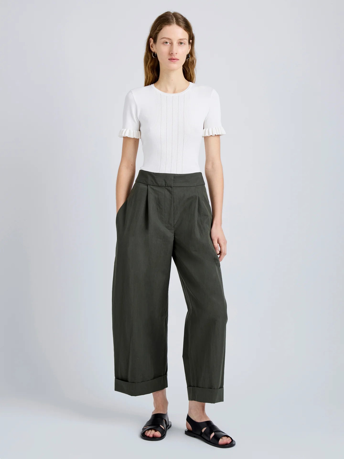 Person wearing a white top and dark green wide-leg pants on a light gray background