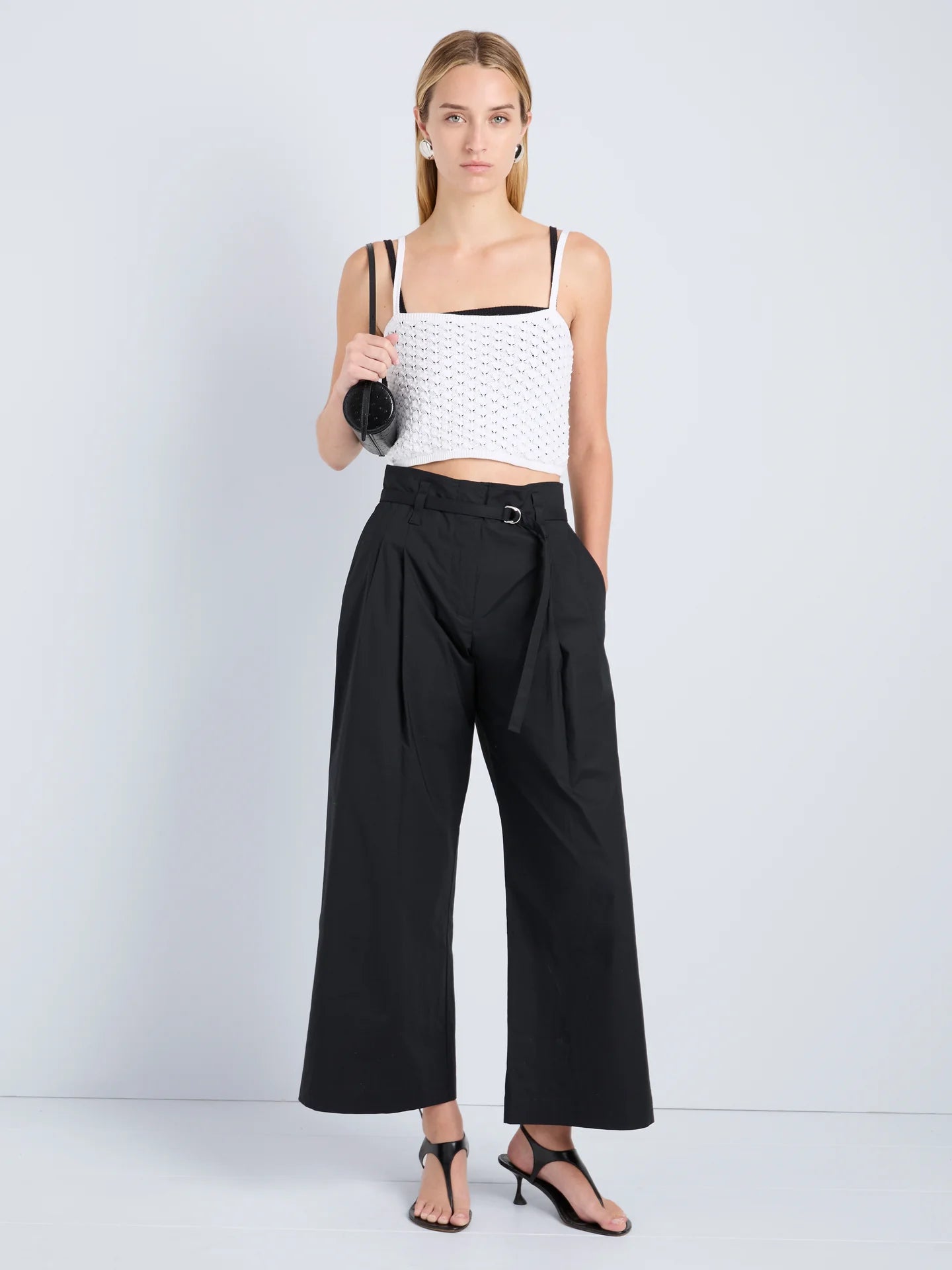 Woman wearing a white top and black wide-leg pants against a light gray background
