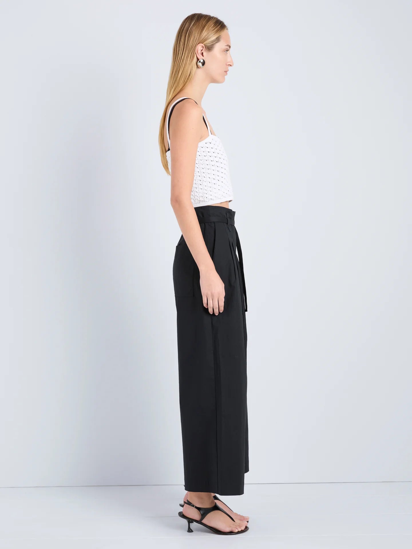 Woman wearing a white top and black wide-leg pants on a light gray background