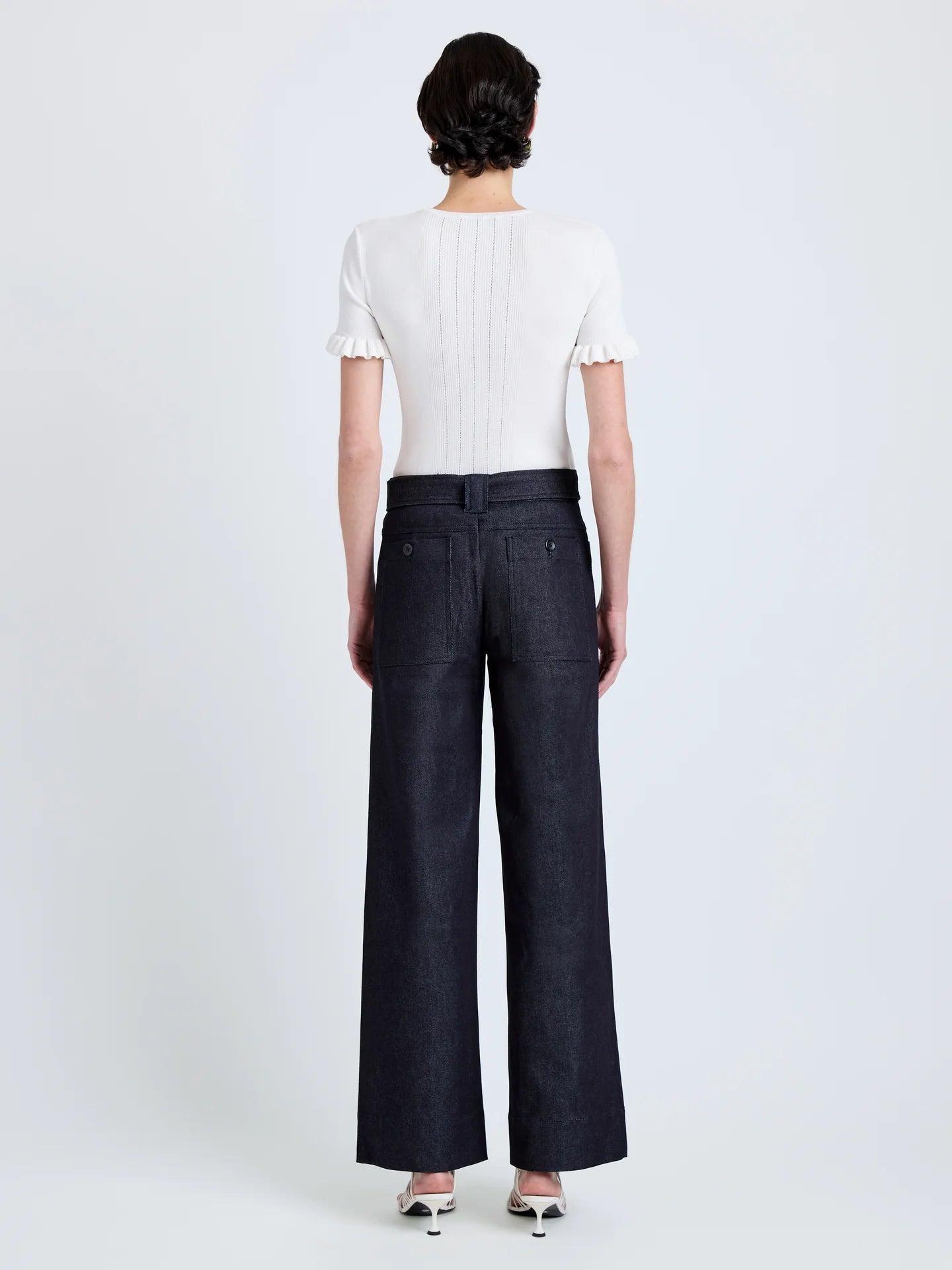 Person wearing a white top and dark blue wide-leg pants on a light gray background