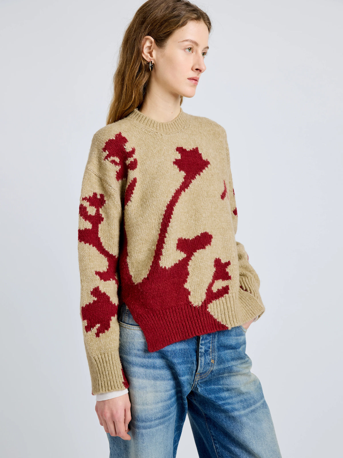 Woman wearing a beige sweater with red floral patterns on a plain background