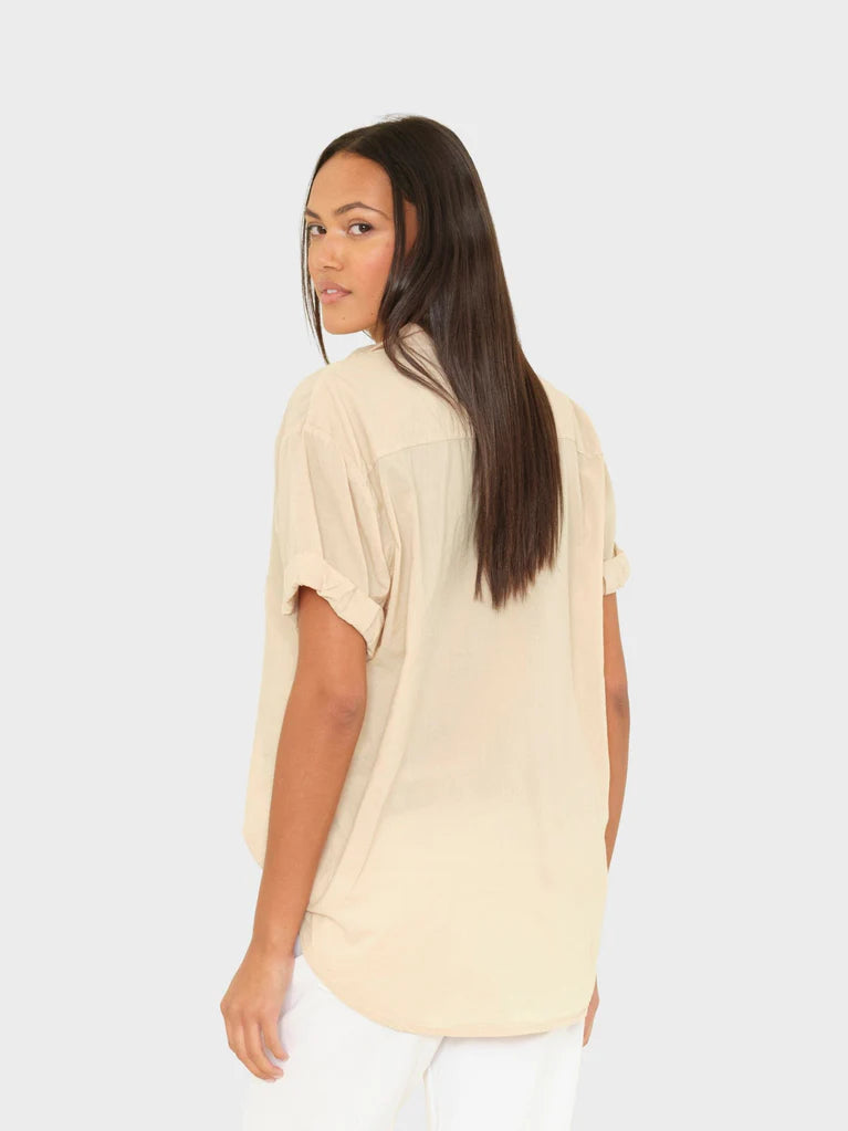 Woman wearing a beige shirt and white pants on a light gray background