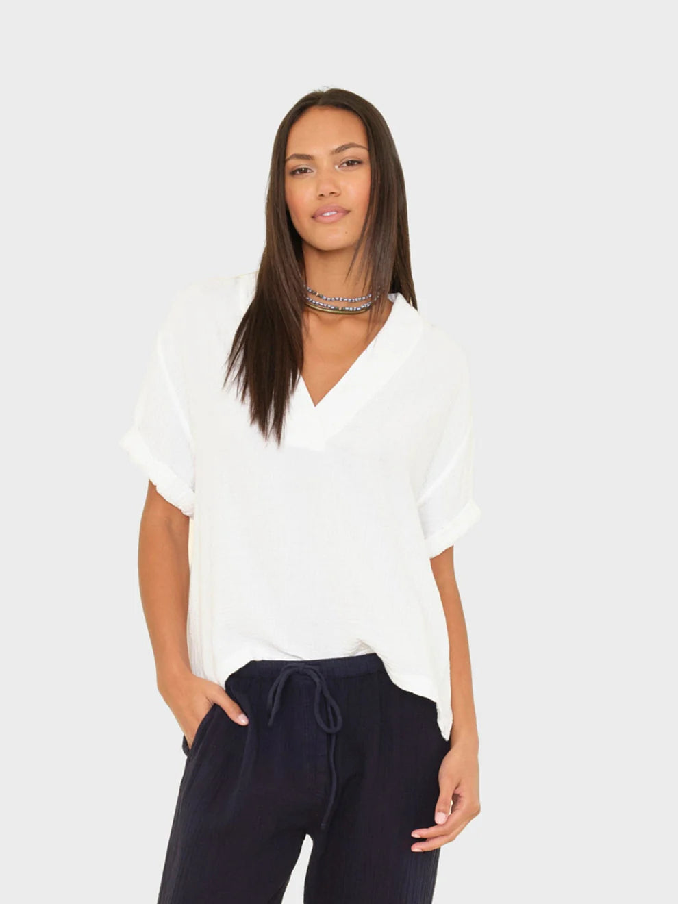 Woman wearing a white blouse and navy pants on a plain background