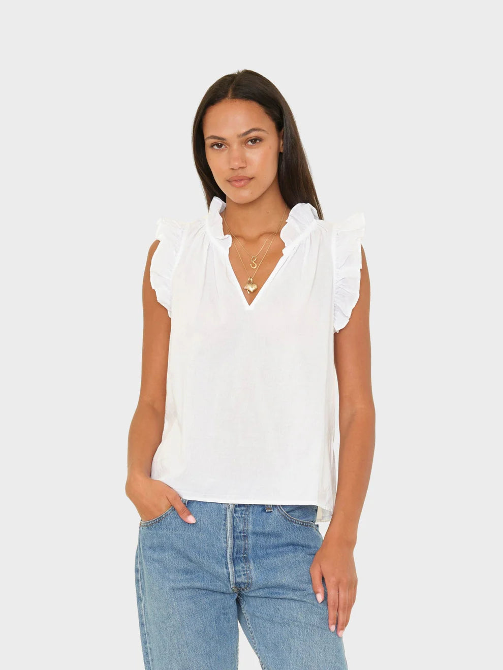 Woman wearing a white blouse with ruffled sleeves and blue jeans on a light gray background