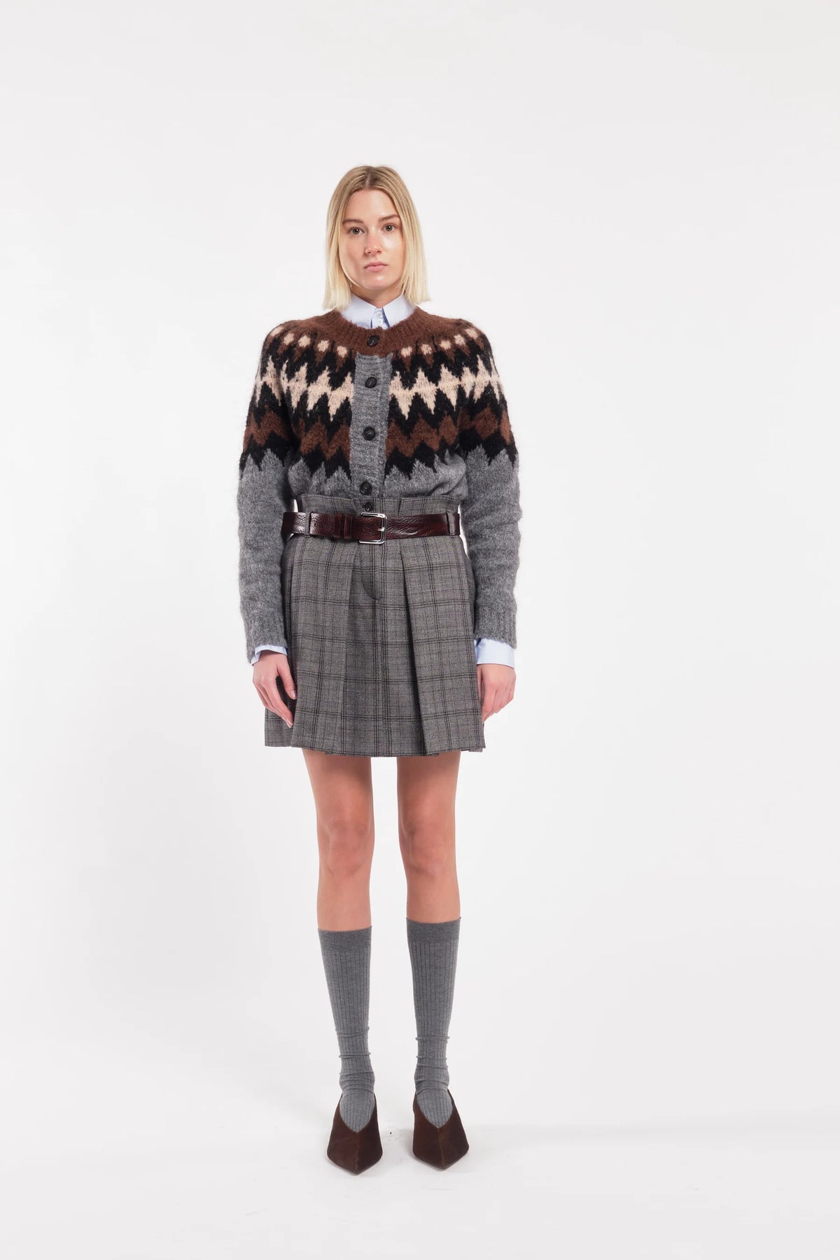 Person wearing a patterned sweater and plaid skirt on a white background