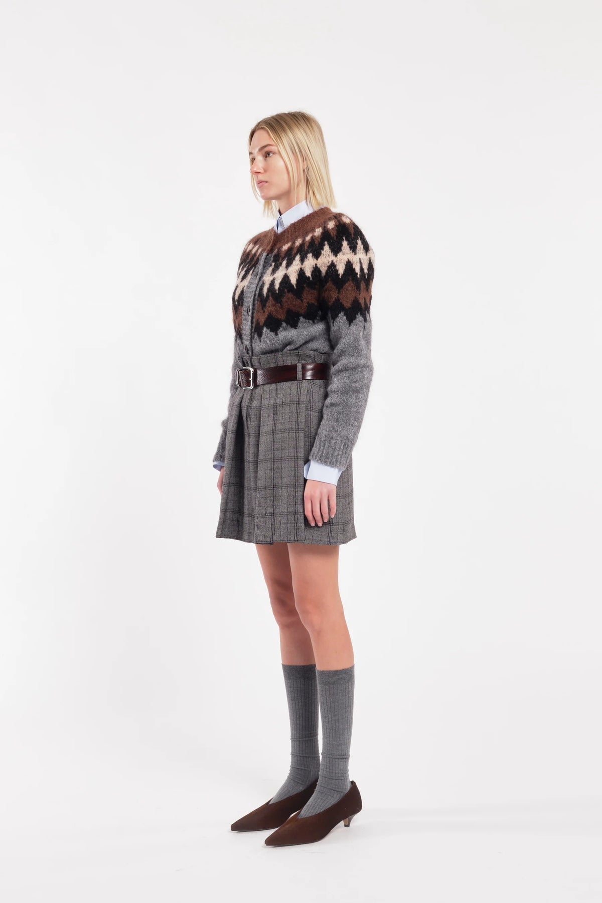 Person wearing a patterned sweater and plaid skirt on a white background